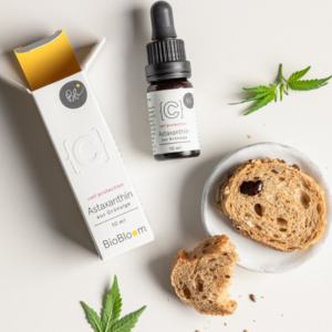 Astaxanthin Tropfen von BioBloom mit Brot und Grünalgenblatt auf hellem Hintergrund.