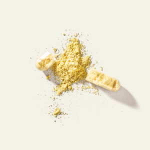 Geöffnete Kapsel mit gelbem Vitamin-B-Pulver auf hellem Hintergrund.