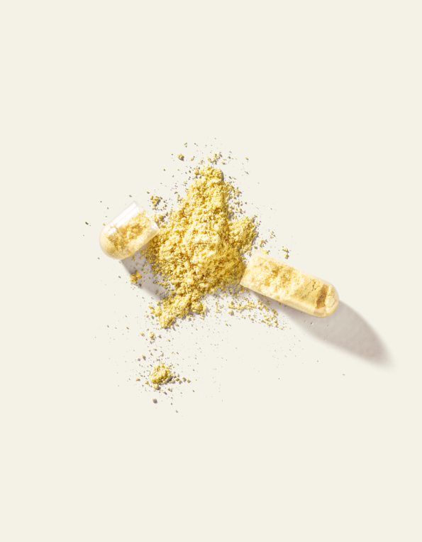 Geöffnete Kapsel mit gelbem Vitamin-B-Pulver auf hellem Hintergrund.