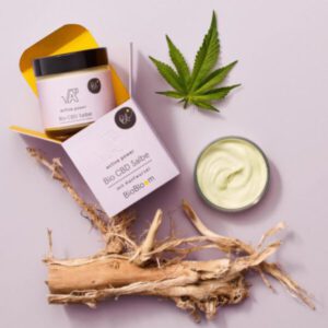 BioBloom Active Power Bio CBD Salbe geöffnet, mit Hanfblatt und Hanfwurzel im Flatlay