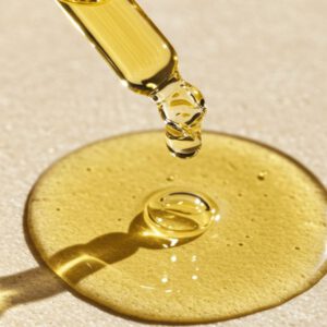 Pipette mit goldgelbem CBD Hautöl boost über einem Öltropfen auf heller Oberfläche.