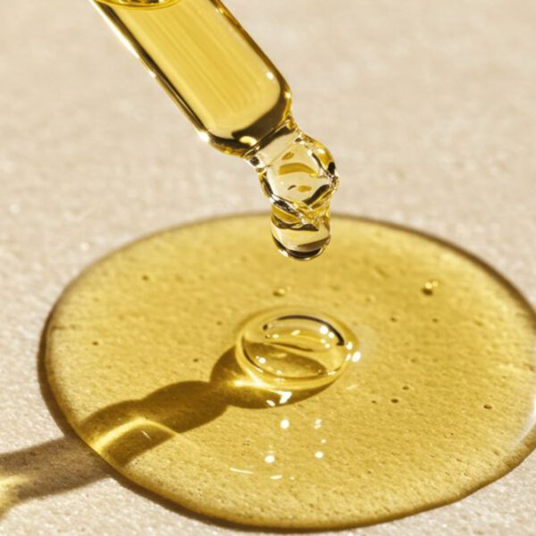 Pipette mit goldgelbem CBD Hautöl boost über einem Öltropfen auf heller Oberfläche.